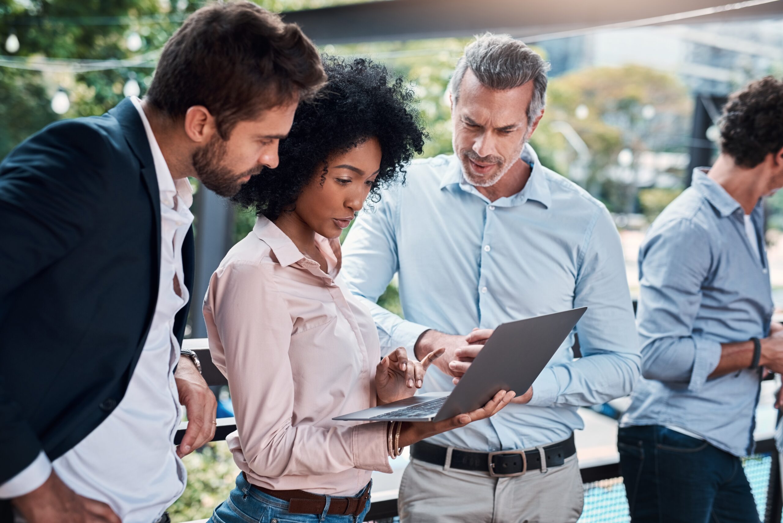 A business professional presenting information on a laptop to clients during an outdoor meeting.
